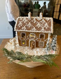 a gingerbread house is decorated with icing and pine branches on a wooden table