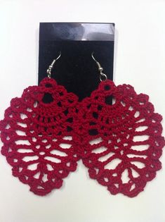 a pair of red crocheted earrings sitting on top of a black stand next to a white wall