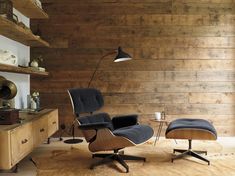 an eames chair and ottoman in front of a wood paneled wall with shelves