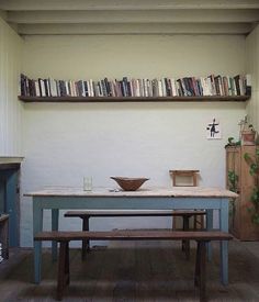 a table and bench in a room with bookshelves on the wall above it