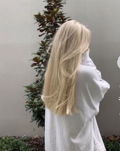 a woman with long blonde hair standing in front of a tree