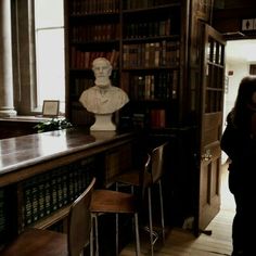 a woman standing in front of a book shelf filled with books next to a bust of abraham lincoln