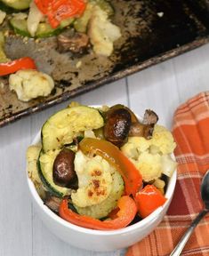 a white bowl filled with vegetables on top of a table next to a tray of food