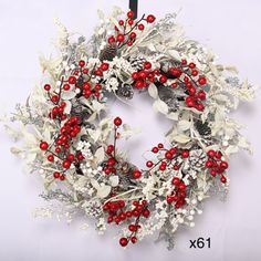 a white wreath with red berries and pine cones hanging on a black metal hook holder