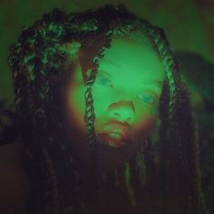 a woman with green light on her face and braids in front of the camera