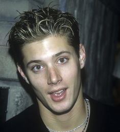 a close up of a person wearing a necklace and looking at the camera with a serious look on his face