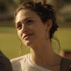 a close up of a person wearing earrings and a white t - shirt with grass in the background