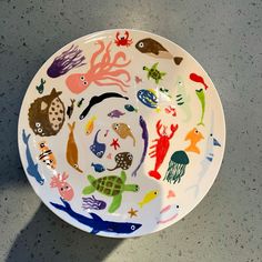 a white plate with colorful sea animals painted on the front and sides, sitting on a gray surface