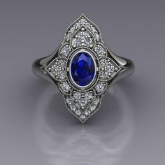 "An oval blue sapphire is set in a bezel in this diamond-studded dinner ring in 14k white gold. The vintage inspired diamond panels are edged with milgrain beading. The top of the ring measures about 20mm at the widest point. Blue Sapphire Dimensions6x4mm EnhancementHeated Carat Weight 0.70 ColorMedium to dark navy blue ClaritySlightly included CutGood PolishGood Diamonds Number22 EnhancementNatural Carat Total Weight0.29 ColorF-G ClaritySI1-2 CutVery Good PolishVery Good This is a custom made item! When you order, we will create a wax model of your ring with our 3D printer. This model is then cast in 14k gold, which is polished and set by hand. This process takes 3-4 weeks, so please allow for this time when ordering if your ring is for a special occasion. Your ring will arrive in a desig Oval Sapphire Diamond Ring In Diamond White, Oval Diamond White Sapphire Ring For Formal Occasions, Oval Sapphire Diamond Ring For Anniversary, Oval Sapphire Ring With Halo Setting In Heirloom Style, Sapphire Oval Diamond Ring For Anniversary, Heirloom Style Oval Sapphire Ring With Diamond, Heirloom Sapphire Oval Diamond Ring, Oval Sapphire Diamond Ring With Accents, Oval Diamond White Sapphire Ring With Halo Setting