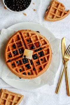 a white plate topped with waffles covered in syrup and blueberries next to goldware