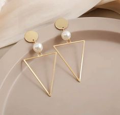 The perfect blend of elegance and modern style - our Geometric Pearl Earrings. Crafted with precision and passion, these earrings are sure to add a touch of sophistication to any outfit.   The intricate shape is carefully crafted to create a visually stunning effect that is both contemporary and timeless. And, to top it all off, each earring features a lustrous pearl that adds a touch of classic elegance.   Our Geometric Pearl Earrings are not just beautiful, but they are also made to last. We use only high-quality materials and expert craftsmanship to ensure that every piece is of the highest standard. And, because we care about the environment, we only use sustainable materials wherever possible. Trendy Gold Triangle Earrings, Elegant Triangle Metal Earrings, Elegant Triangle Metal Jewelry, Elegant Triangle-shaped Jewelry, Triangle Metal Earrings For Gift, Trendy Hypoallergenic Wedding Earrings, Trendy Hypoallergenic Earrings For Wedding, Trendy Metal Pearl Drop Earrings, Elegant Triangle Earrings For Formal Occasions