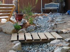 a small garden area with rocks, gravel and wooden steps leading up to a bench