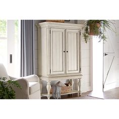 a white armoire in a living room next to a couch and potted plant