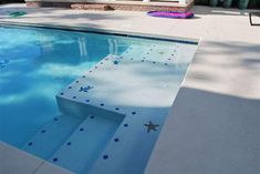 an empty swimming pool with blue tiles and starfish designs on the bottom edge, in front of a house