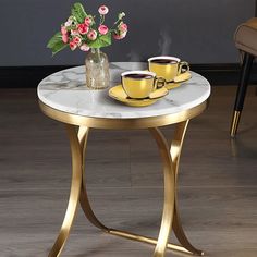 two cups of coffee sit on a marble top table with gold legs and a vase filled with flowers