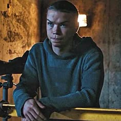 a young man sitting in front of a camera next to a wooden table with a light on it