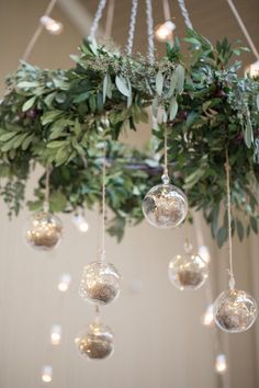 a chandelier filled with glass balls and greenery hanging from it's ceiling