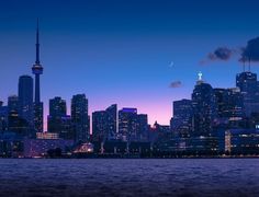 the city skyline is lit up at night as seen from across the water with clouds in the sky