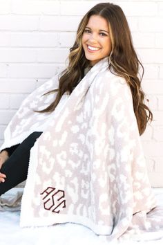 a smiling woman sitting on top of a bed under a white and brown animal print blanket