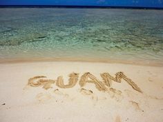 the word gum written in sand on a beach with clear blue ocean water behind it