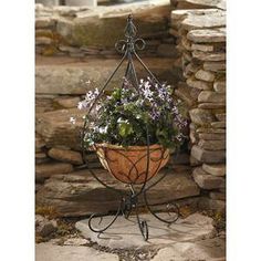 a potted planter with flowers hanging from it's stand on a stone wall