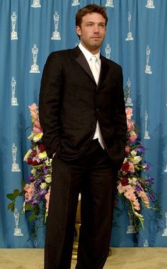 a man in a tuxedo standing next to a blue curtain with flowers on it