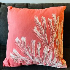 a coral colored pillow with white embroidered corals on the front and back, sitting on a black couch