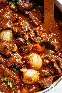 a pot filled with beef and potatoes on top of a wooden spoon in a sauce