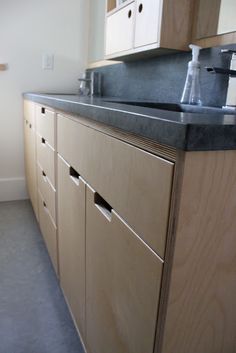 a kitchen with wooden cabinets and black counter top next to a white wall in the background