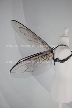 a white mannequin wearing a black and silver dragonfly headpiece with wings