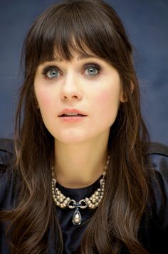 a woman with long hair wearing a black shirt and pearls around her neck is looking at the camera