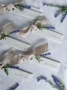 four personalized name tags with lavender flowers and ribbon tied around them on a white tablecloth