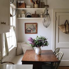 a wooden table topped with a vase filled with purple flowers next to a white wall