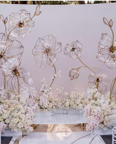 an arrangement of white flowers and greenery in front of a pink wall with gold accents