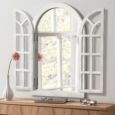 a white vase with pink flowers sitting on top of a wooden table next to a mirror