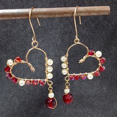 a pair of red and white beaded heart shaped earrings on top of a wooden stick