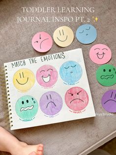 a child's hand holding a notebook with colored paper emoticions on it