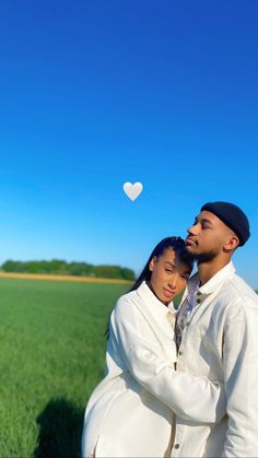 a man and woman standing next to each other in a field with a heart shaped balloon