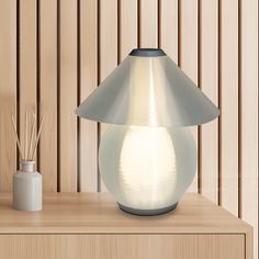 a white lamp sitting on top of a wooden table next to a vase and reeds