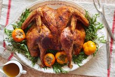 a roasted turkey on a platter with oranges and herbs next to a cup of tea