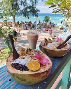 two coconut bowls filled with food on top of a blue table next to the ocean