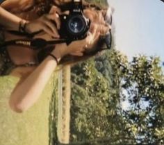 a woman taking a photo with her camera on the grass in front of some trees