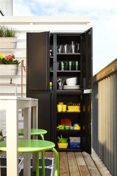 an outdoor storage cabinet on the back of a deck with green table and chairs around it