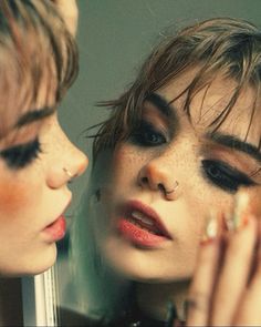 two women with makeup and piercings looking at each other's eyes in front of a mirror