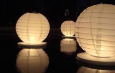 three white paper lanterns sitting on top of a black table next to each other in the dark