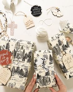 two hands holding wrapped gift boxes on a table with other wrapping materials and tags around them