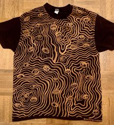 a t - shirt with an abstract design on the front and back, sitting on a wooden floor