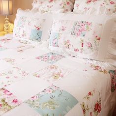 a white bed with pink and blue flowers on the comforter next to a night stand