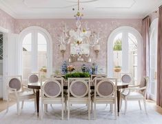 an elegant dining room with pink walls and white chairs, chandelier over the table