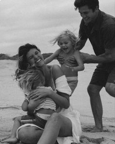 a woman and two children are sitting on the beach with their arms around each other